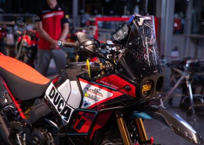 Close-up of the 2024 Ducati DesertX Rally motorcycle, highlighting its distinctive features and branding against a desert backdrop.